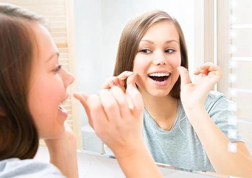 Young woman flossing her teeth in front of a bathroom mirror
