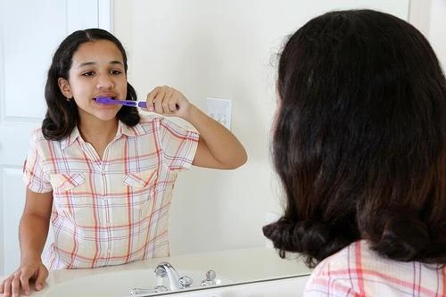 Girl brushing her teeth at a bathroom mirror as part of a daily routine to prevent cavities
