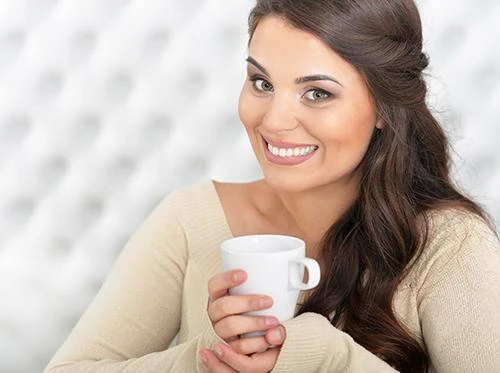 Woman holding a warm drink, sipping fluids through the day to ease dry mouth